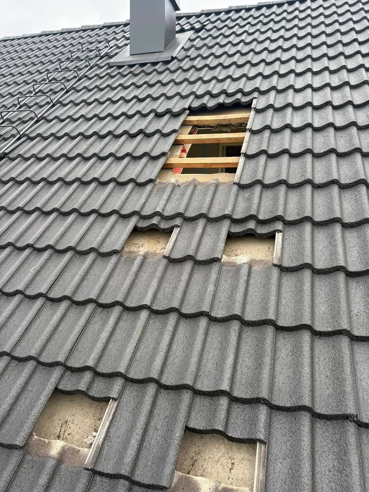 Skadade takpannor med synliga hål och underliggande takstol av trä.